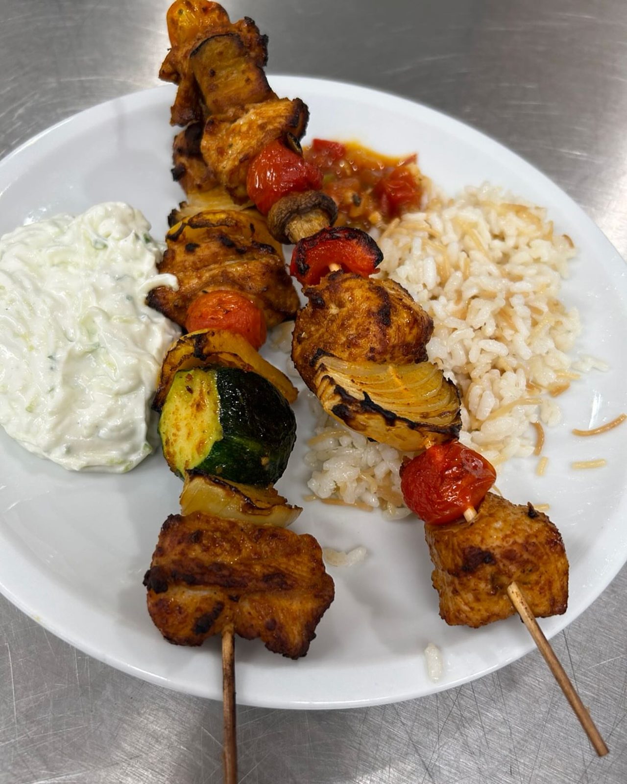 Bunte Fleischspieße mit Reis, Grillgemüse und Tzatziki auf einem Teller